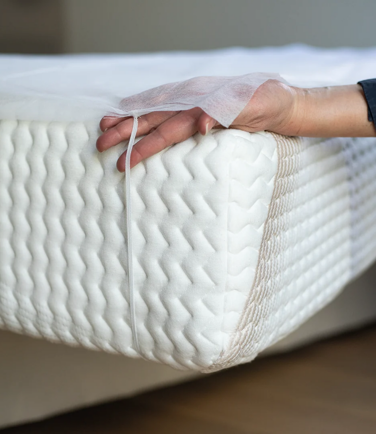 Main ajustant un protège-matelas jetable à élastique sur le coin d'un matelas blanc matelassé, vue rapprochée