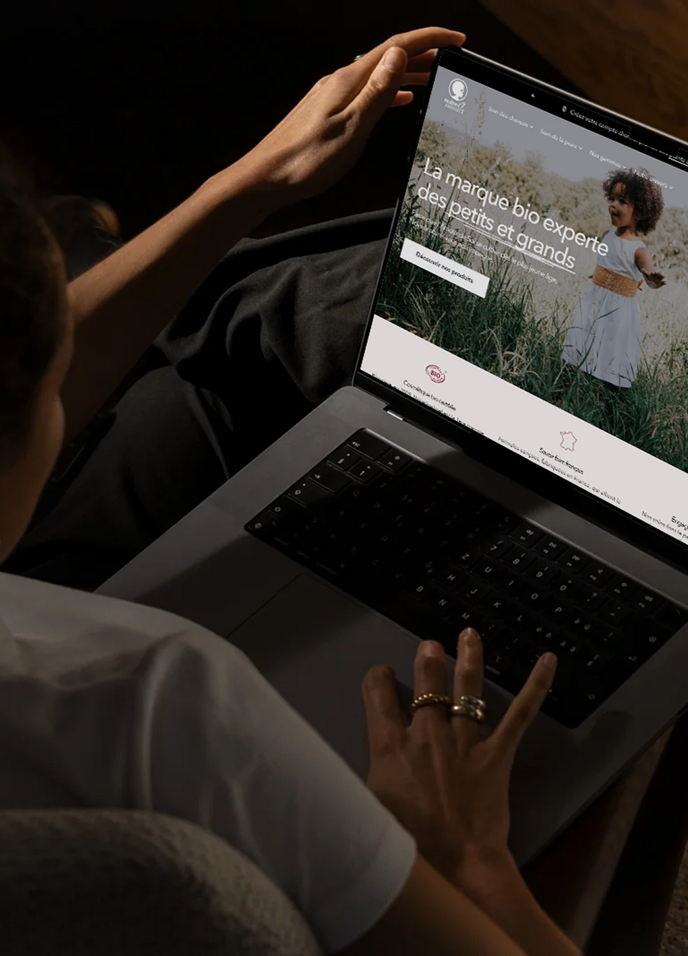 Femme parcourant sur un ordinateur portable le site Noire O Naturel, « La marque bio experte des petits et grands », enfant dans l'herbe