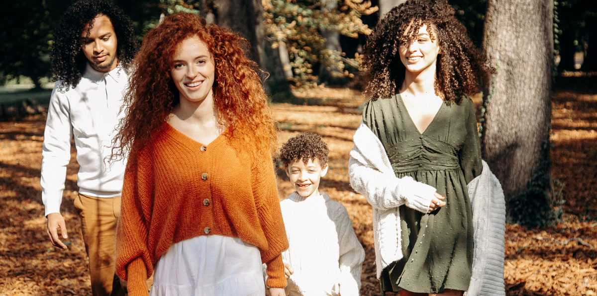 Groupe de quatre personnes aux cheveux bouclés, dont un enfant, souriant en marchant dans un parc aux feuilles d'automne
